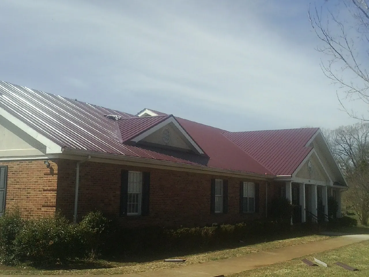 Red metal roof with gabled entries on a long brick building, from a Hail Damage Roof Repair job in Far Rockaway
