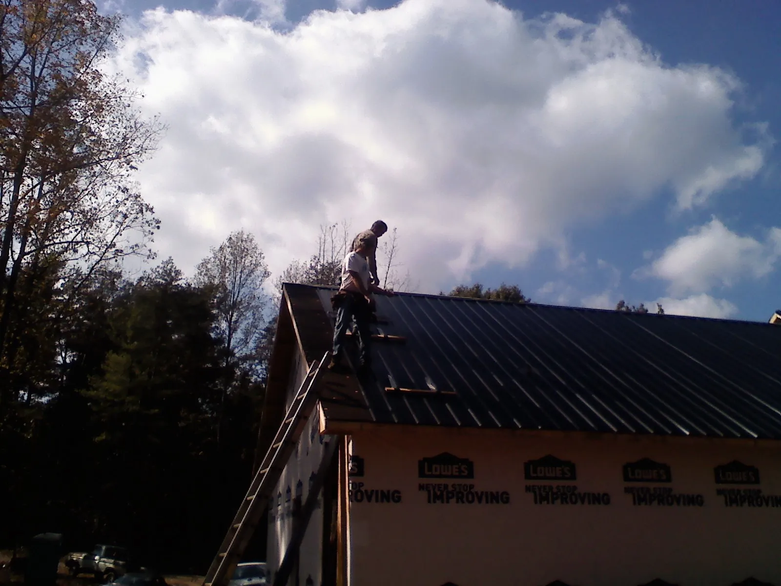 Roofer fastening dark metal panels high against a cloudy sky, from a Roof Inspection job in Far Rockaway