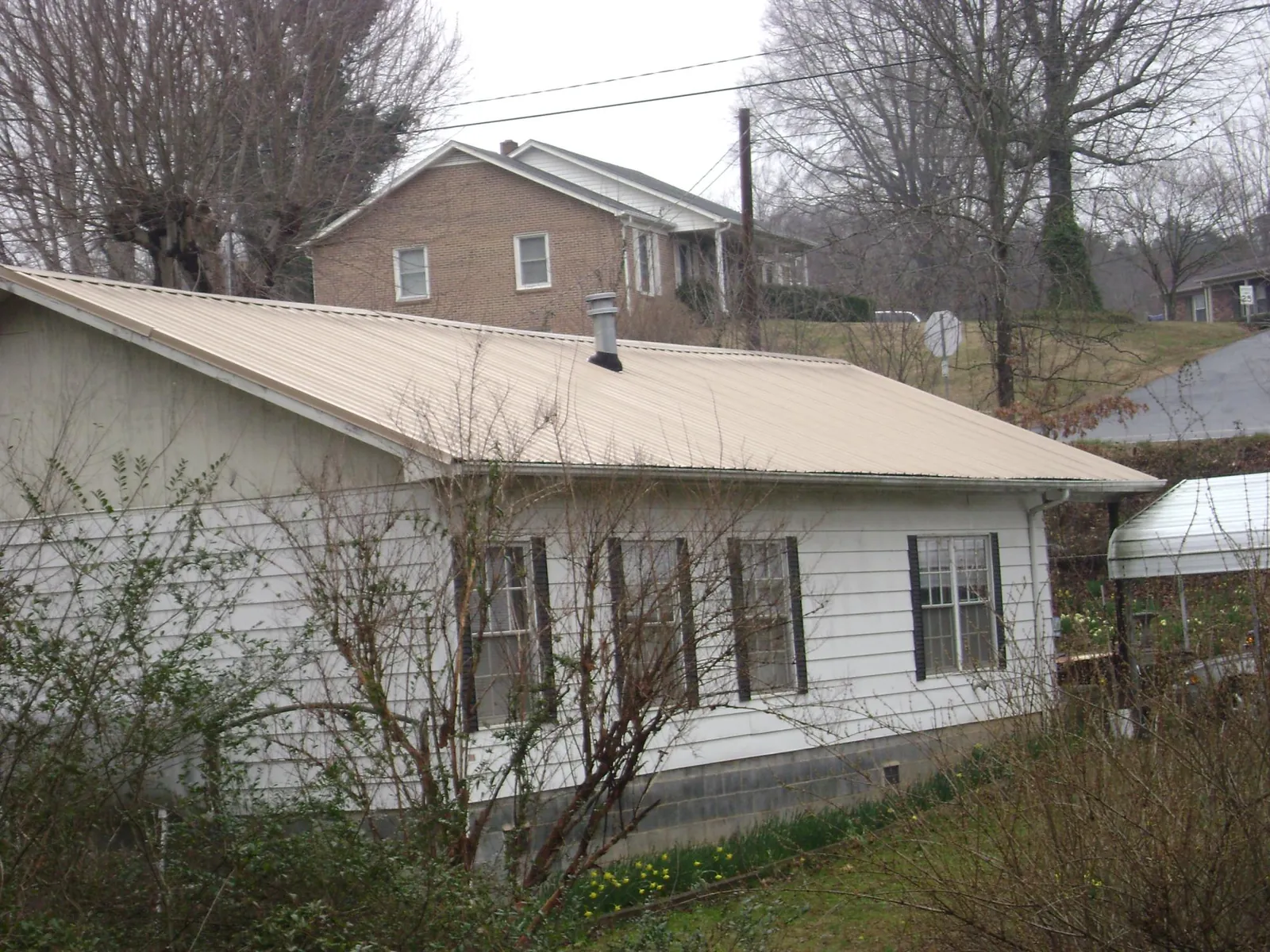 Tan metal roof on a white sided house set into a hillside — Commercial Roofing by Roofing Brothers in Far Rockaway